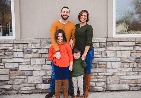 Mother father and two kids smiling together in front of dental office