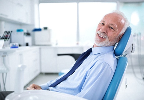 An older gentleman sitting back in a dentist’s chair preparing to learn about dental implant care in Geneva