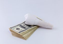 Model of dental implant resting on a stack of money