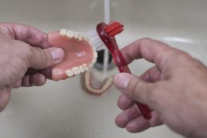 a person brushing their dentures in a sink